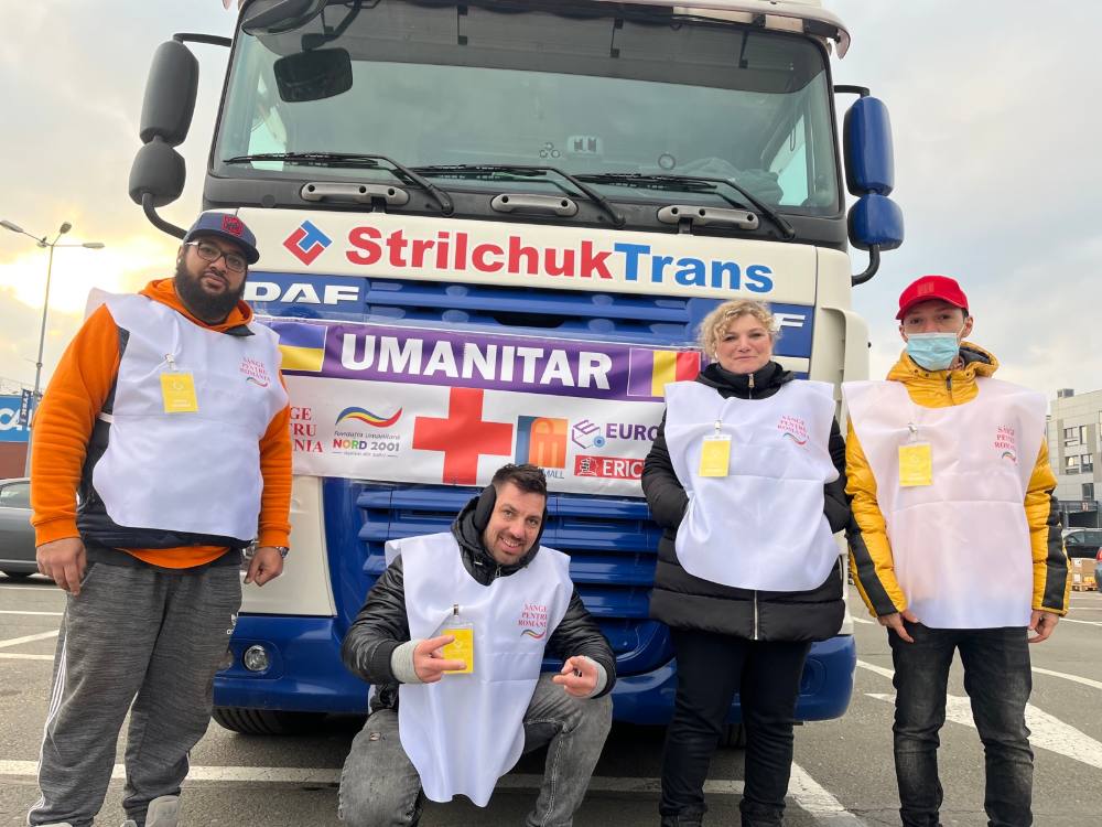 Voluntari în veste albe în fața unui camion cu ajutoare umanitare