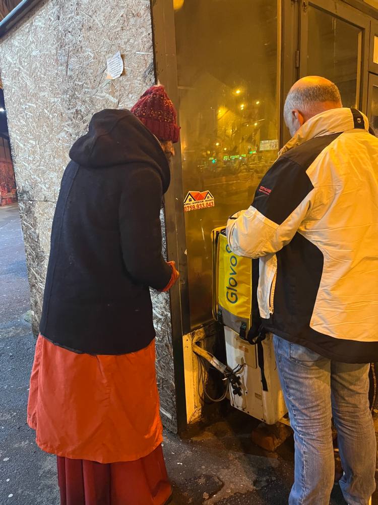 Voluntară care dă mâncare unui om, noaptea, lângă o ușă luminată