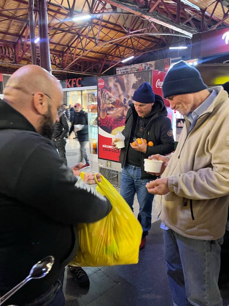 Voluntar care împarte supă caldă dintr-o sacoșă galbenă, în Gara de Nord