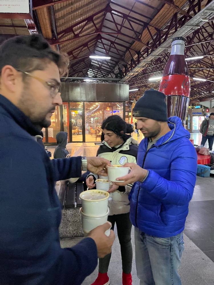 Voluntar care dă un pahar cu supă caldă unui bărbat în geacă albastră, în holul Gării de Nord
