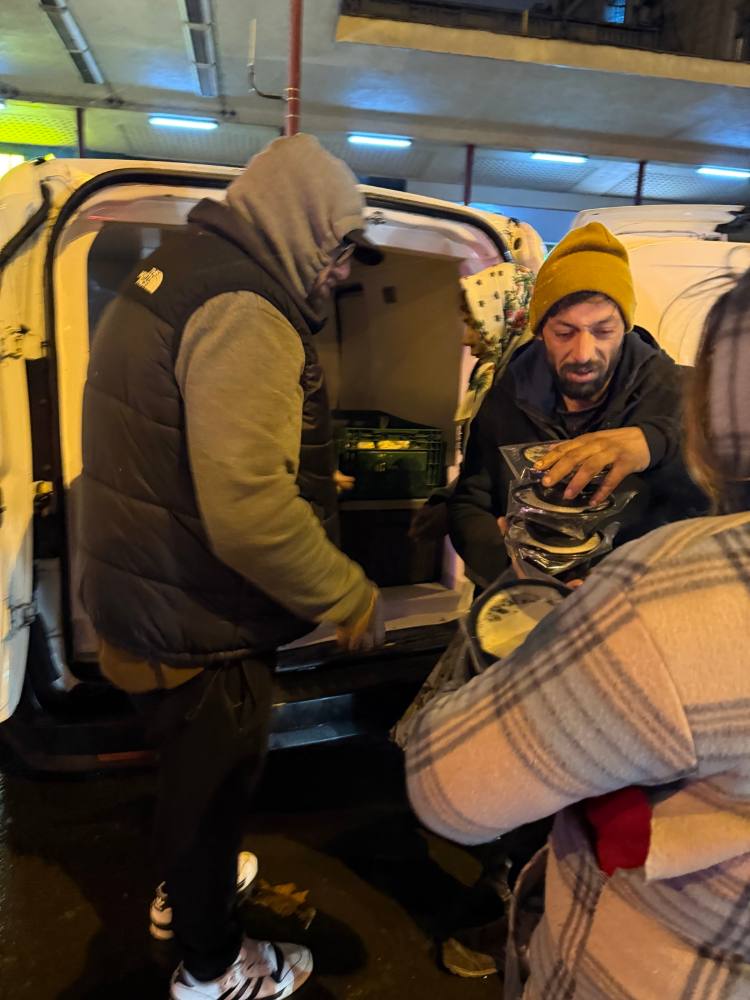 Voluntari care împart porții calde din portbagajul unei mașini, noaptea