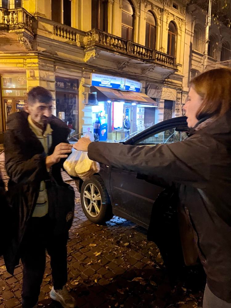 Voluntară care dă o porție caldă unui om pe stradă, seara