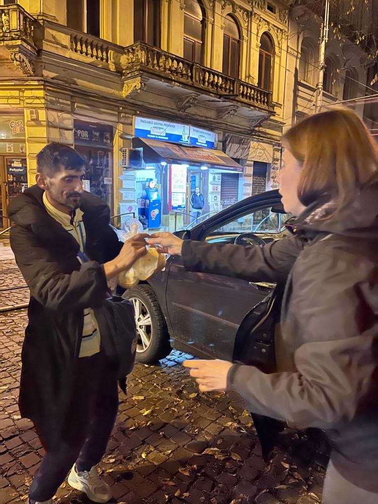 Voluntară care dă o porție caldă unui bărbat pe o stradă din centrul Bucureștiului, seara