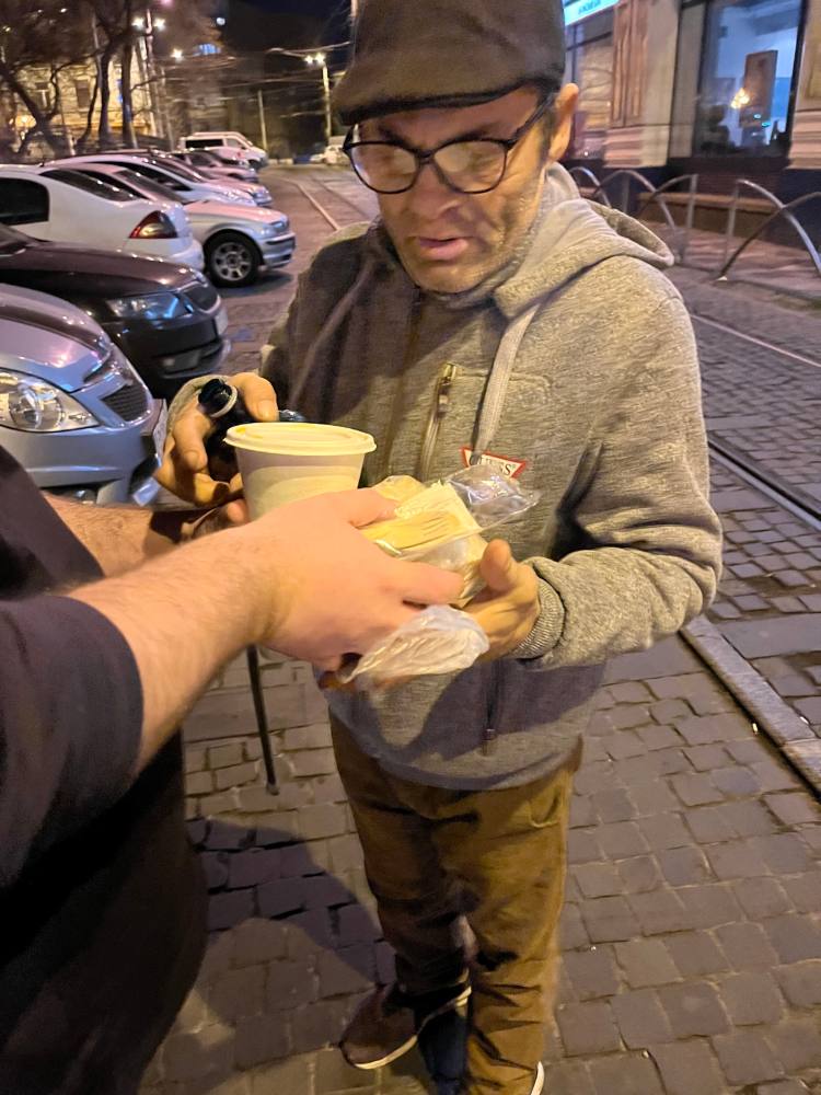 Bărbat cu șapcă primește o cană de supă caldă pe stradă
