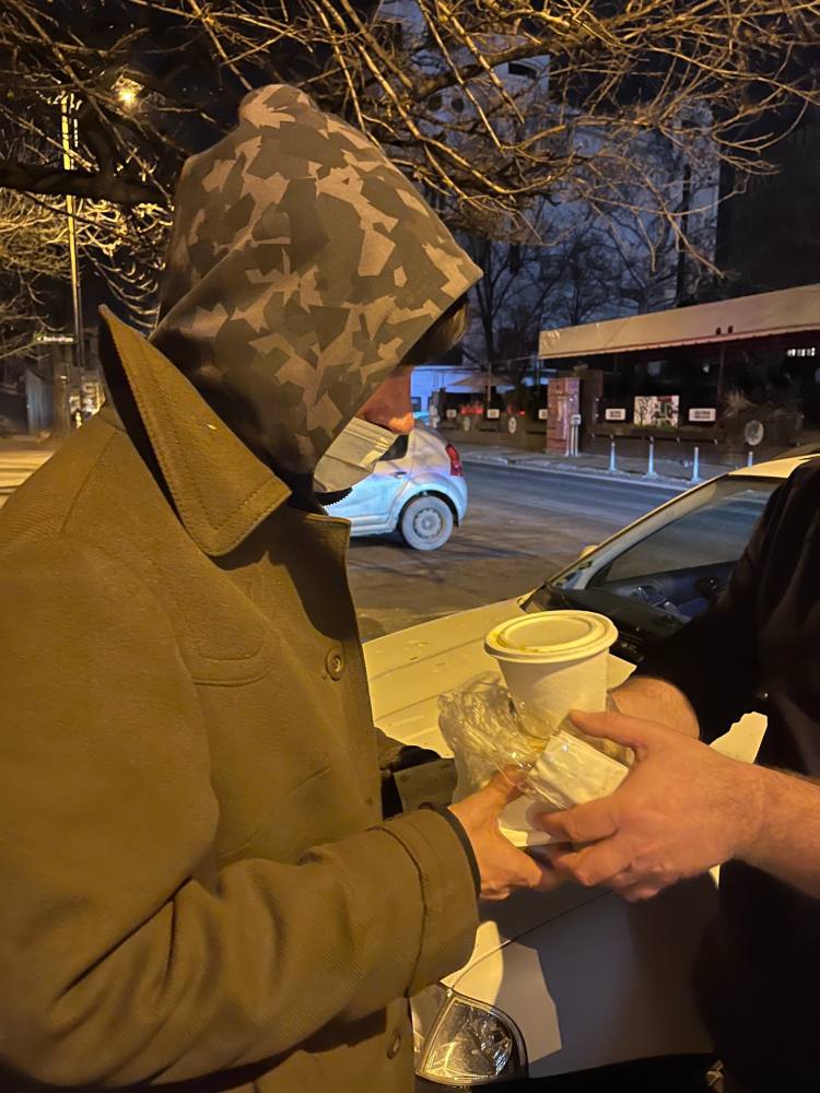 Om cu glugă care primește un pahar cu supă caldă, noaptea, pe stradă
