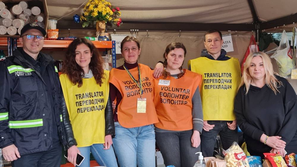 Echipa de voluntari în veste galbene și portocalii, lângă cortul cu mâncare